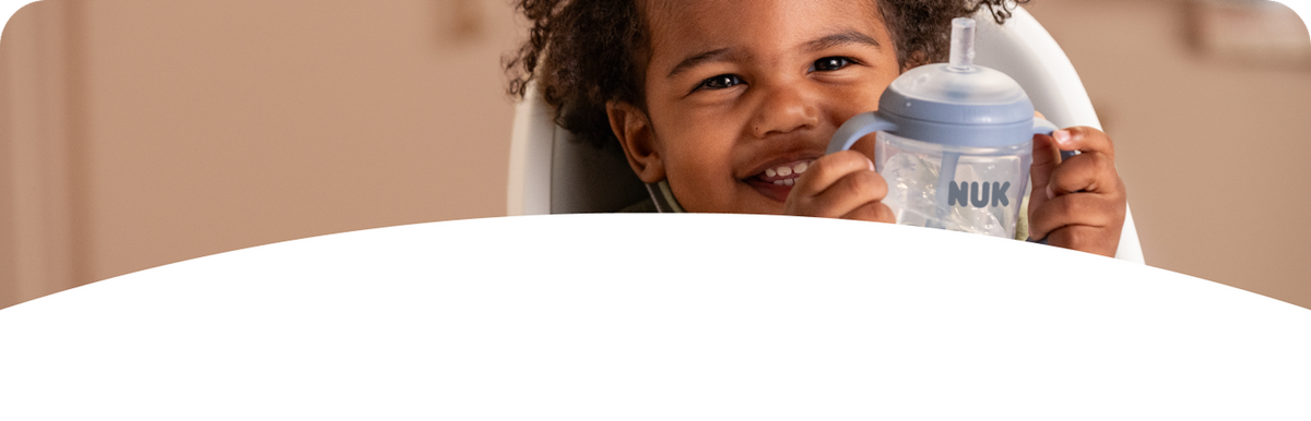 Smiling toddler drinking from a NUK learner cup