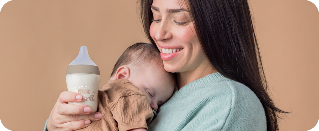 Parent cuddling their baby with a NUK bottle